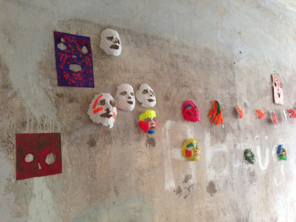 Bemalte Gipsmasken hängen an einer Wand.